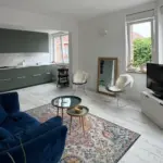 Studio ouvert renove avec canape bleu, cuisine verte et grandes fenetres